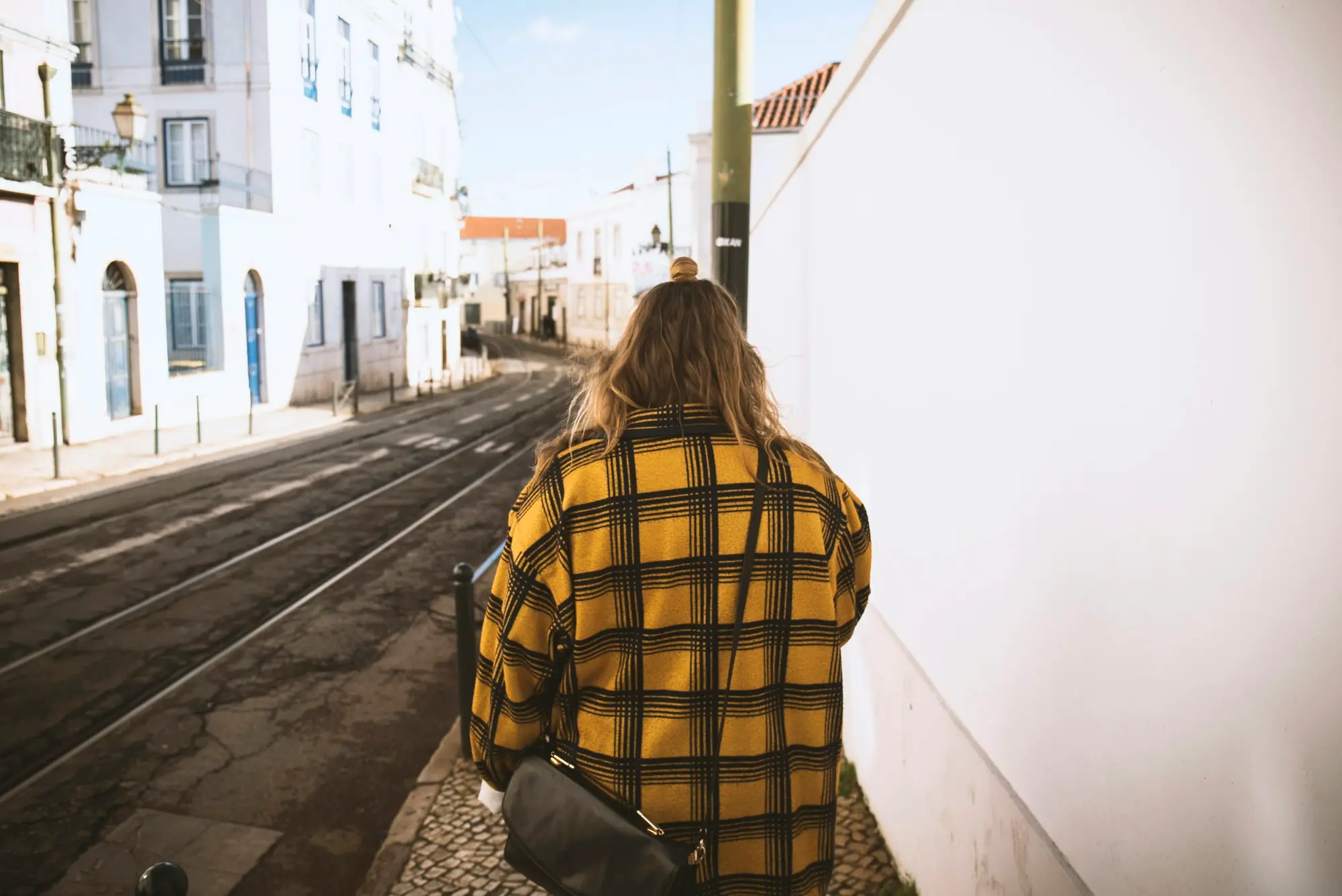 A woman walking alone with a crossbody bag down a quiet European street lined with pale buildings