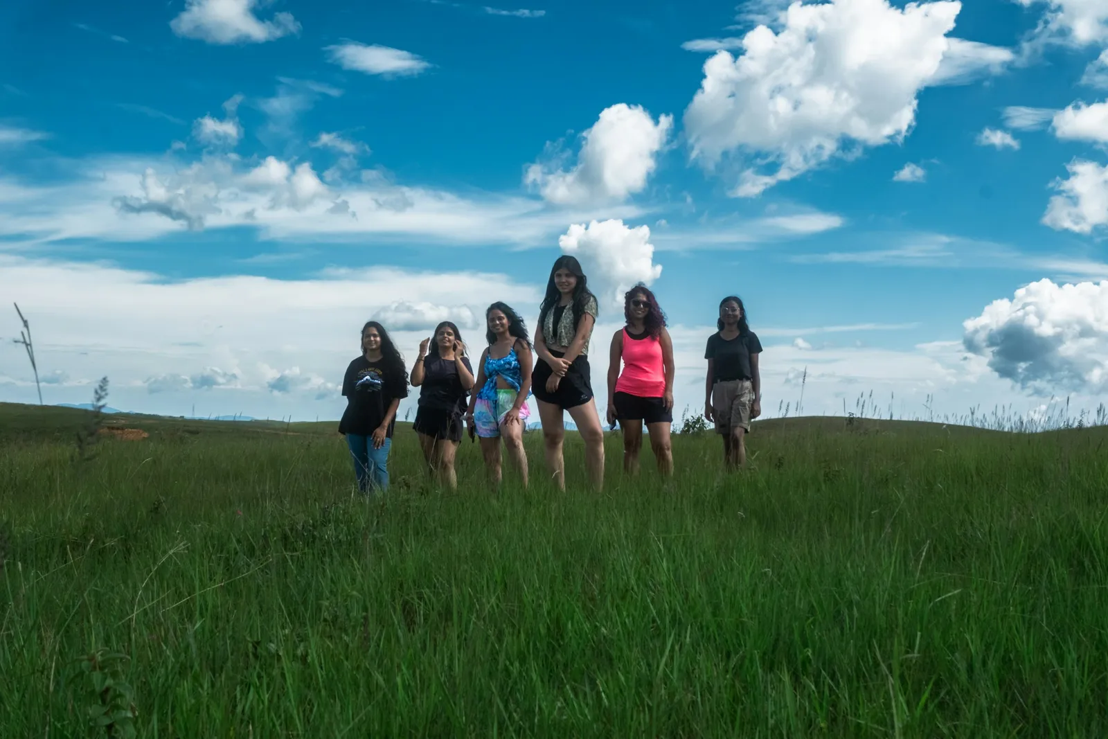 A group of women standing together in a green field under a bright blue sky on a trip