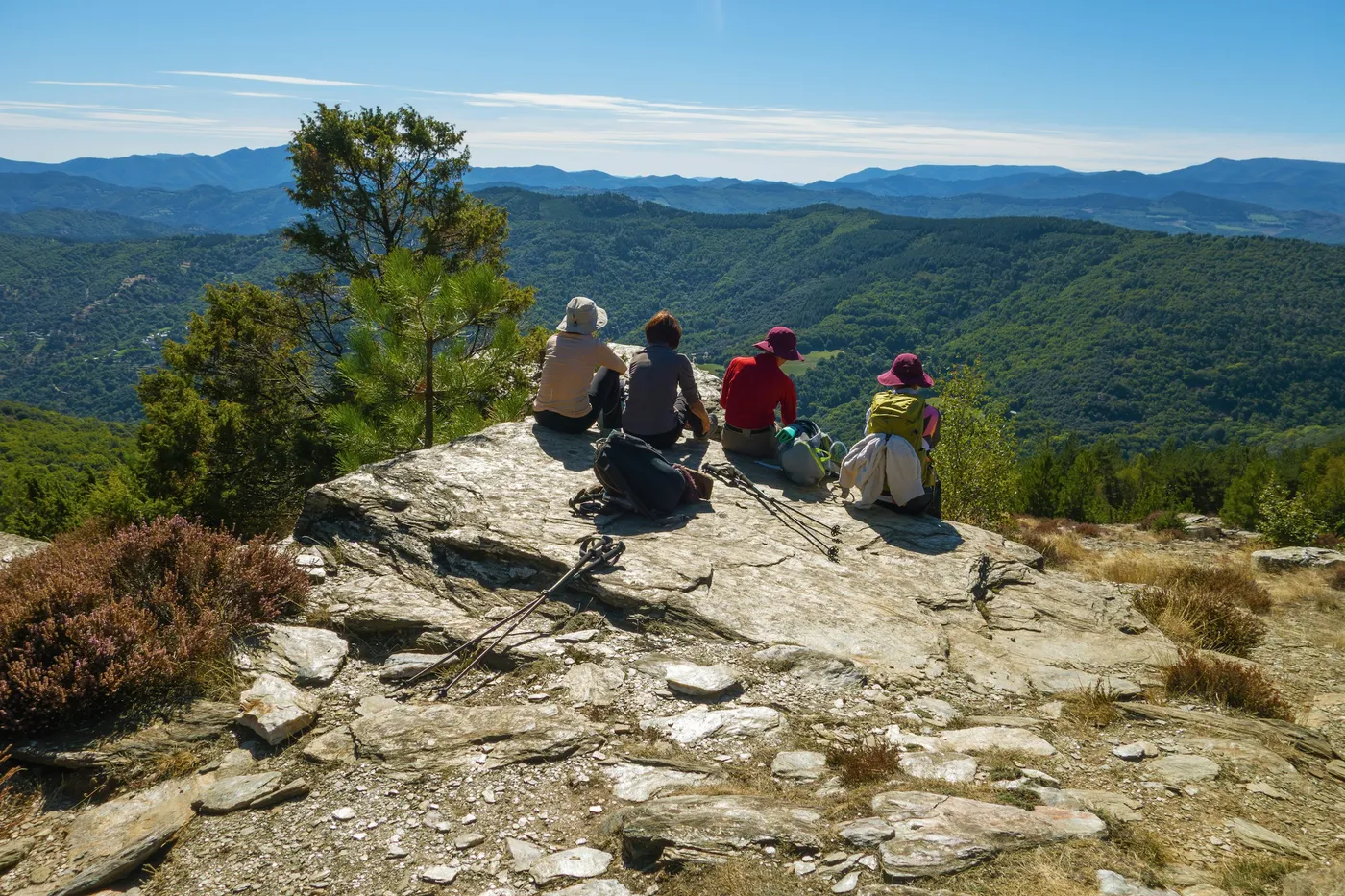 A small group of women hikers resting on a rocky summit overlooking green hills on a walking tour